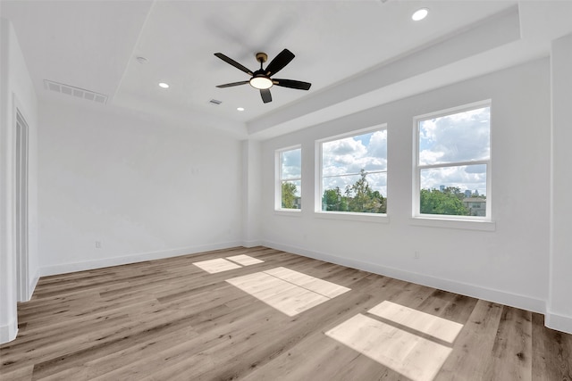 unfurnished room with a raised ceiling, light wood-style flooring, a ceiling fan, baseboards, and visible vents