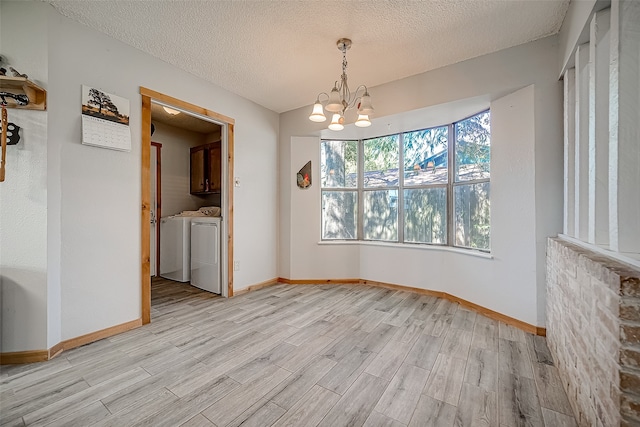 unfurnished dining area with a textured ceiling, washing machine and dryer, light hardwood / wood-style flooring, and a chandelier