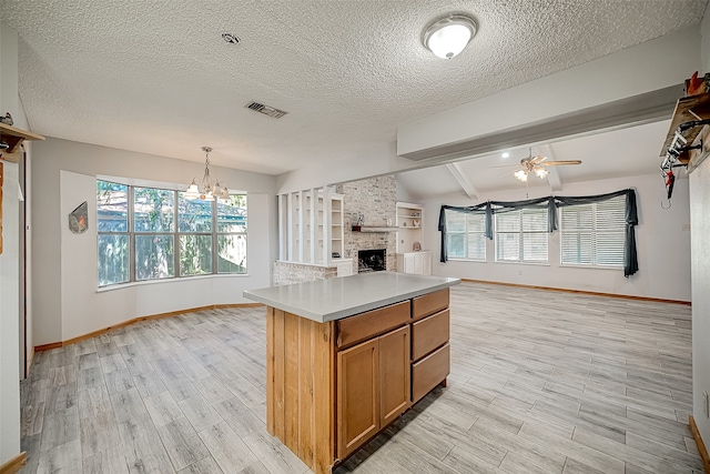 kitchen with pendant lighting, light hardwood / wood-style floors, a fireplace, a kitchen island, and ceiling fan with notable chandelier