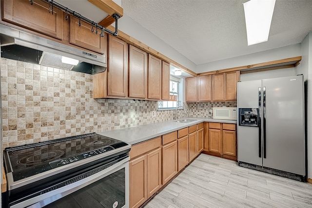 kitchen featuring sink, stainless steel appliances, tasteful backsplash, a textured ceiling, and light wood-type flooring