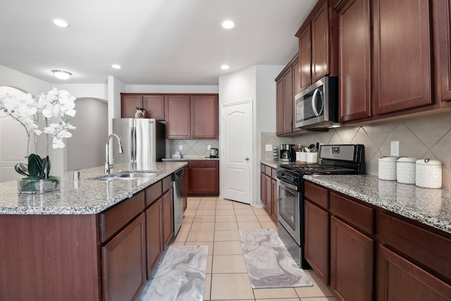 kitchen featuring light stone counters, stainless steel appliances, backsplash, and a center island with sink