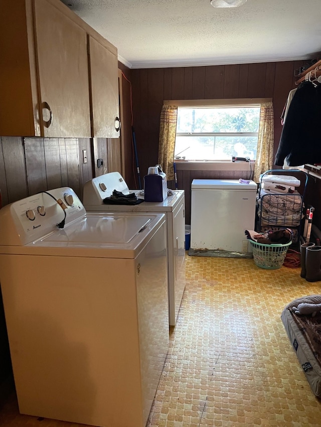 laundry room with wood walls, a textured ceiling, cabinets, and washing machine and clothes dryer