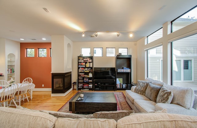 living room featuring a multi sided fireplace, track lighting, and light wood-type flooring