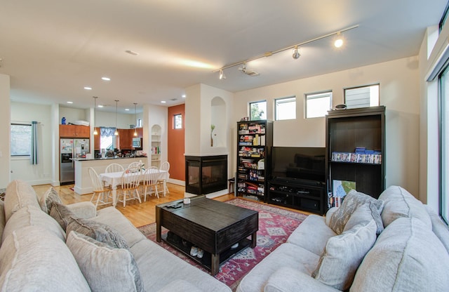 living room featuring a multi sided fireplace, track lighting, and light hardwood / wood-style flooring