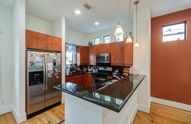 kitchen featuring hanging light fixtures, appliances with stainless steel finishes, kitchen peninsula, and light wood-type flooring