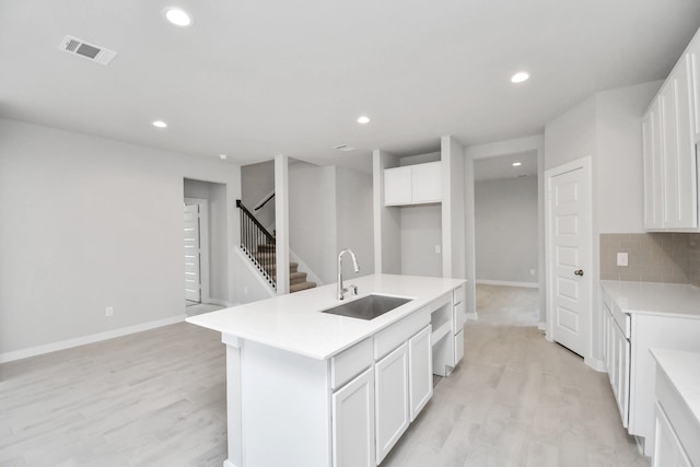 kitchen with white cabinetry, sink, light wood-type flooring, and a center island with sink