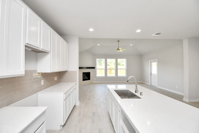 kitchen with sink, backsplash, white cabinetry, ceiling fan, and light hardwood / wood-style flooring