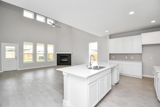 kitchen with a kitchen island with sink, light hardwood / wood-style floors, sink, white cabinets, and a towering ceiling