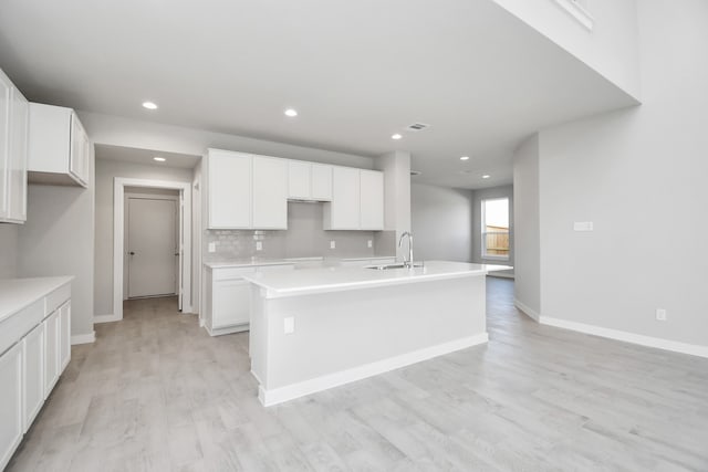 kitchen featuring white cabinets, tasteful backsplash, an island with sink, light hardwood / wood-style floors, and sink