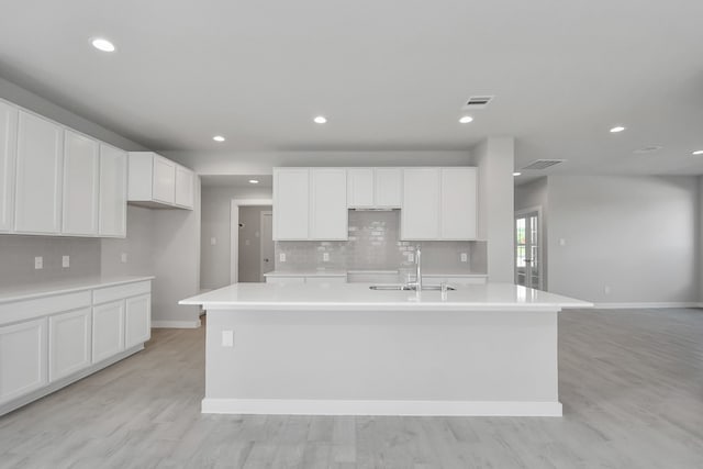 kitchen with sink, a kitchen island with sink, light hardwood / wood-style flooring, and white cabinets