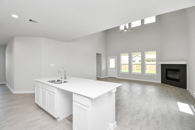 kitchen featuring a kitchen island with sink, sink, light wood-type flooring, white cabinetry, and a towering ceiling