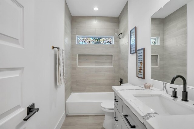 full bathroom with hardwood / wood-style floors, vanity, tiled shower / bath combo, and toilet