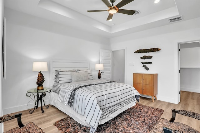 bedroom with light hardwood / wood-style floors, a raised ceiling, and ceiling fan