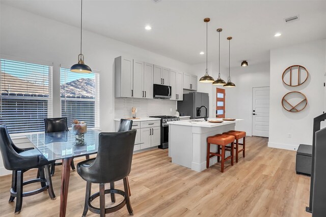 kitchen with decorative light fixtures, decorative backsplash, stainless steel appliances, and a kitchen island with sink