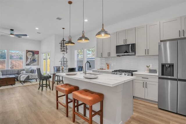 kitchen featuring appliances with stainless steel finishes, ceiling fan, a kitchen island with sink, sink, and pendant lighting