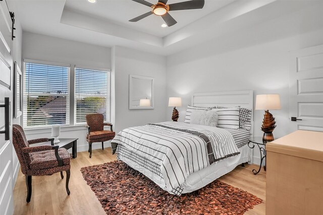 bedroom with a tray ceiling, ceiling fan, and light hardwood / wood-style floors