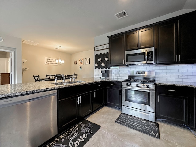 kitchen with light stone countertops, sink, stainless steel appliances, decorative light fixtures, and light tile patterned floors