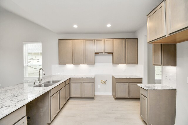 kitchen with tasteful backsplash, sink, light stone counters, and light hardwood / wood-style flooring