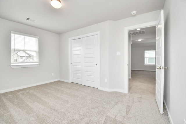 unfurnished bedroom with light colored carpet, multiple windows, and a closet