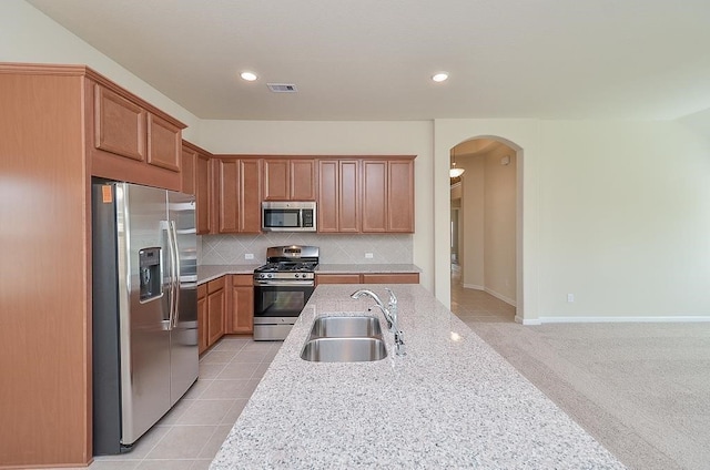 kitchen with sink, decorative backsplash, light stone countertops, appliances with stainless steel finishes, and light tile patterned flooring