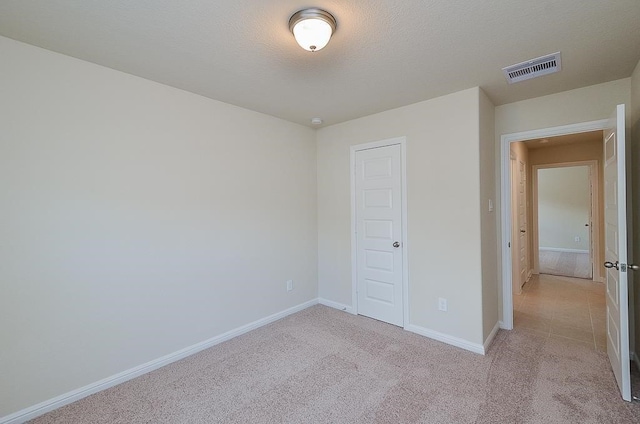 unfurnished bedroom featuring a textured ceiling, light colored carpet, and a closet