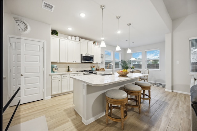 kitchen with a kitchen island with sink, white cabinetry, decorative light fixtures, and stainless steel appliances