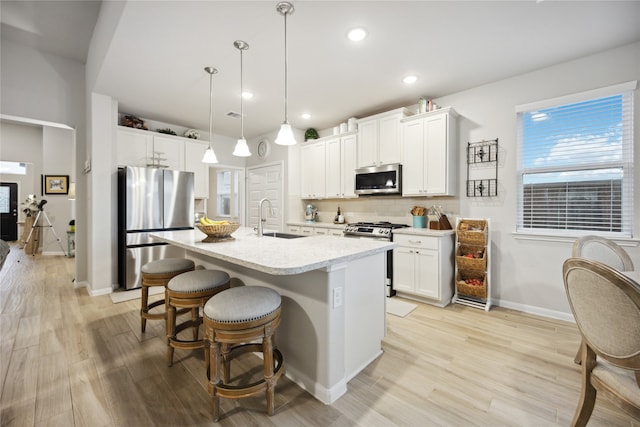 kitchen featuring a kitchen island with sink, hanging light fixtures, sink, white cabinetry, and appliances with stainless steel finishes