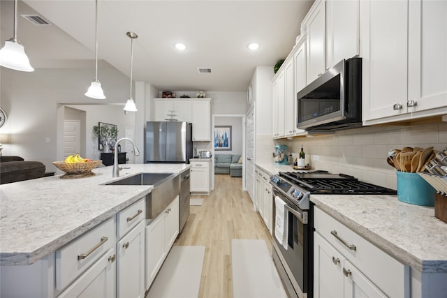 kitchen with stainless steel appliances, a center island with sink, decorative light fixtures, white cabinetry, and tasteful backsplash