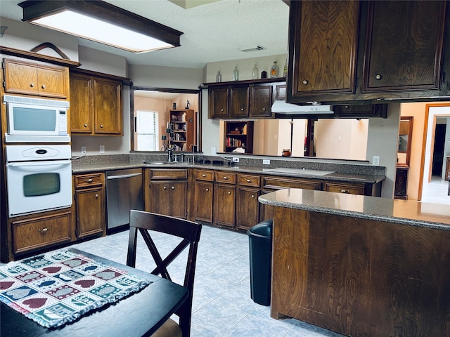 kitchen featuring sink, a textured ceiling, dark brown cabinets, white microwave, and stainless steel dishwasher