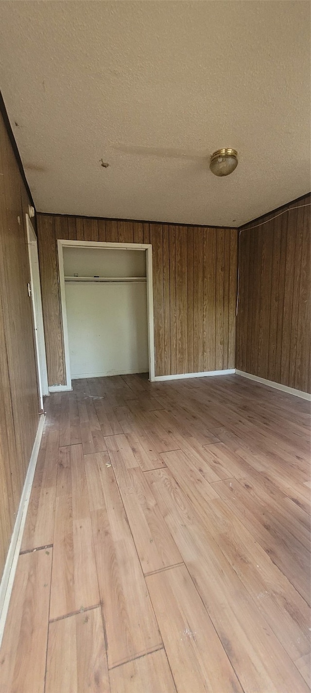 empty room with wood walls, a textured ceiling, and light wood-type flooring