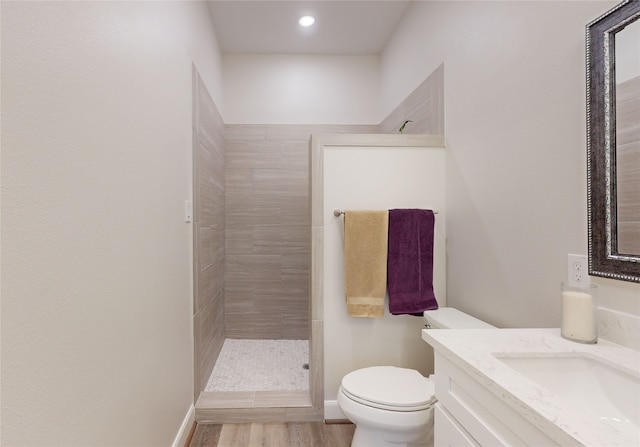 bathroom featuring vanity, hardwood / wood-style floors, a tile shower, and toilet