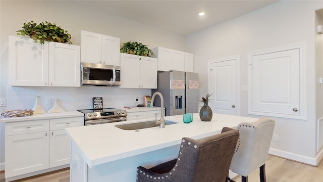 kitchen with sink, an island with sink, white cabinetry, stainless steel appliances, and a breakfast bar area