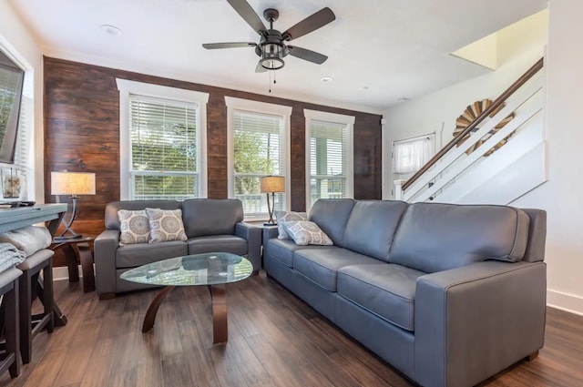 living room featuring dark wood-type flooring, wooden walls, and ceiling fan