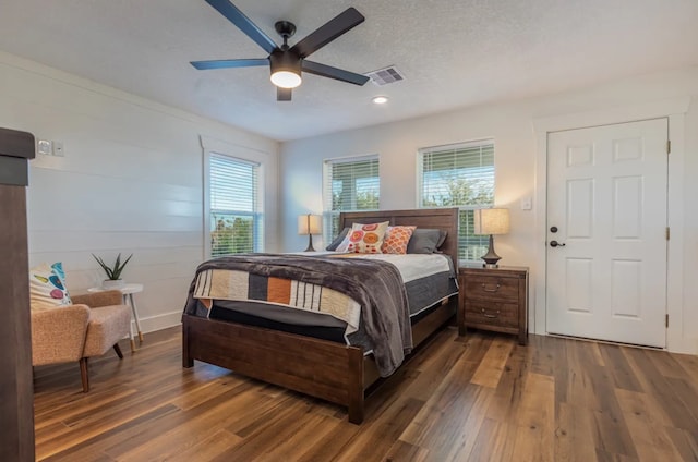 bedroom featuring ceiling fan, wood walls, a textured ceiling, and dark hardwood / wood-style floors