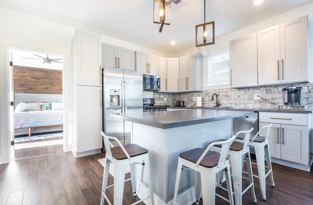 kitchen with backsplash, appliances with stainless steel finishes, a breakfast bar, dark hardwood / wood-style flooring, and decorative light fixtures