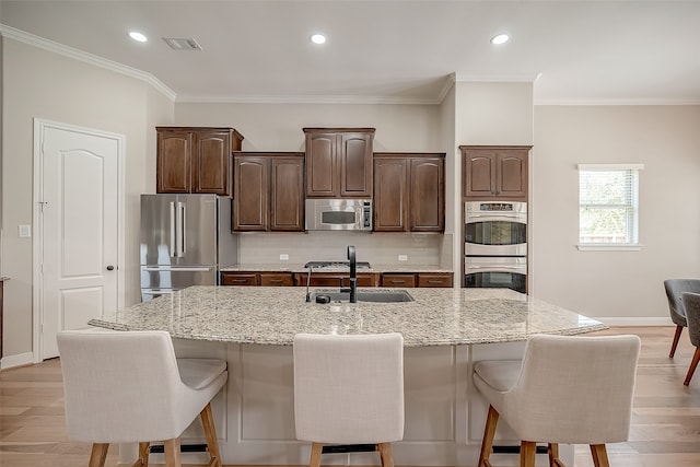 kitchen with light hardwood / wood-style floors, stainless steel appliances, decorative backsplash, and an island with sink