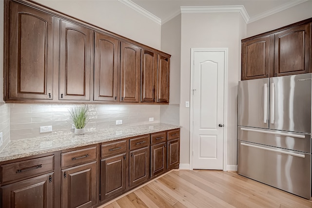 kitchen with stainless steel fridge, backsplash, light stone countertops, ornamental molding, and light hardwood / wood-style floors