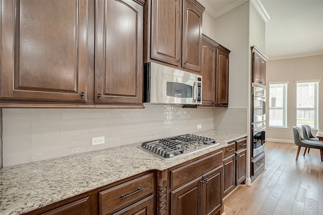 kitchen with decorative backsplash, appliances with stainless steel finishes, light wood-type flooring, ornamental molding, and light stone counters