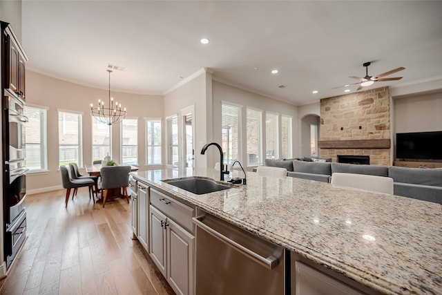 kitchen featuring sink, light wood-type flooring, stainless steel dishwasher, light stone counters, and ornamental molding