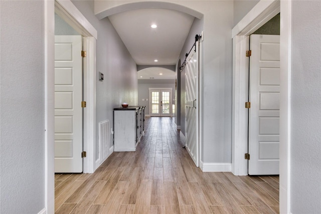 hallway with light wood-style floors, baseboards, recessed lighting, a barn door, and arched walkways