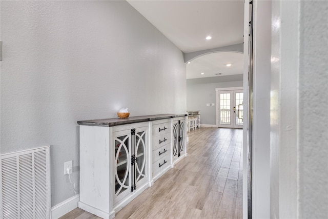 hallway with visible vents, arched walkways, light wood finished floors, and baseboards