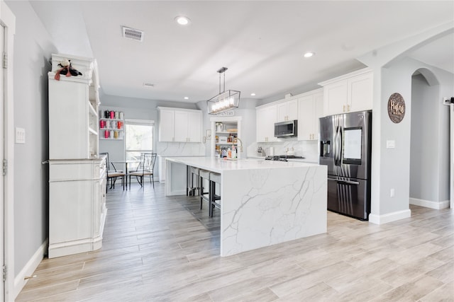 kitchen with white cabinetry, a kitchen island with sink, light hardwood / wood-style flooring, pendant lighting, and stainless steel appliances