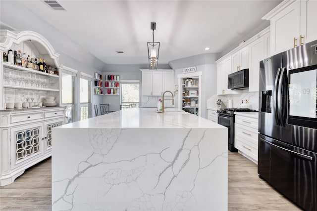 kitchen featuring black appliances, a kitchen island with sink, and white cabinetry