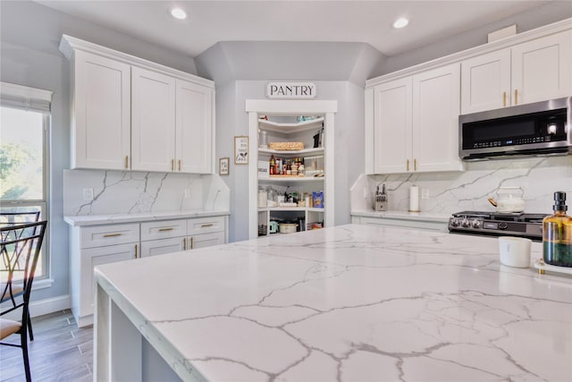 kitchen featuring tasteful backsplash, light stone counters, stainless steel microwave, recessed lighting, and white cabinetry