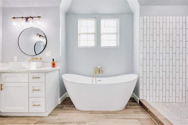 full bath featuring vanity, baseboards, a soaking tub, and wood finish floors
