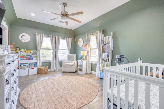 bedroom featuring visible vents, vaulted ceiling, wood finished floors, baseboards, and a crib