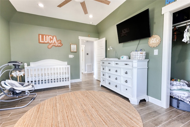 bedroom featuring a nursery area, wood-type flooring, a closet, and ceiling fan