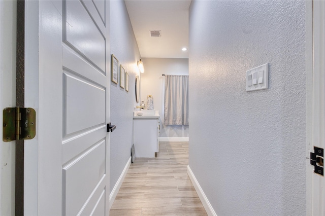 hallway featuring baseboards, a textured wall, light wood-type flooring, and visible vents