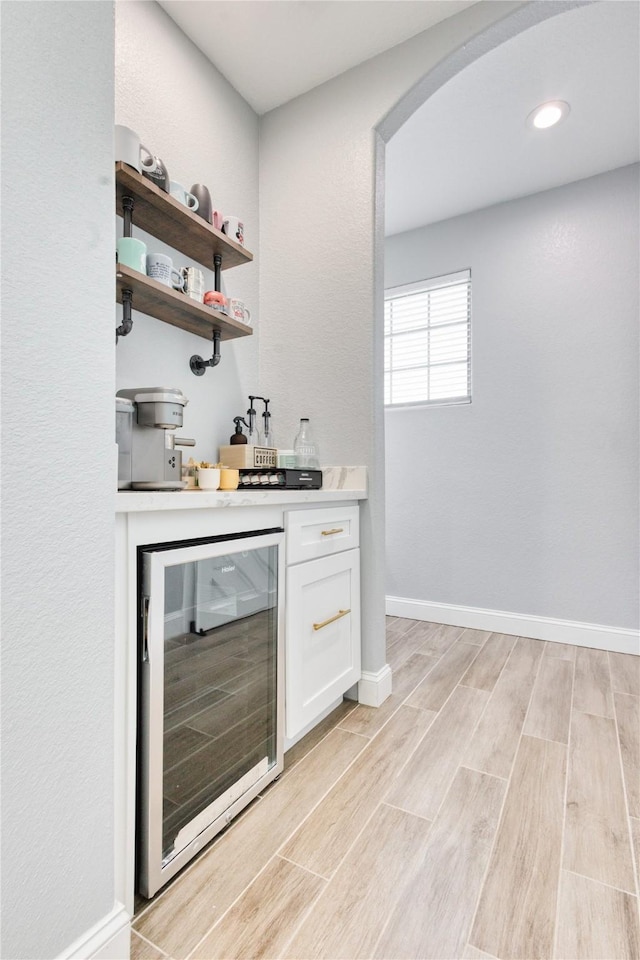 bar featuring arched walkways, a dry bar, baseboards, beverage cooler, and light wood-style floors