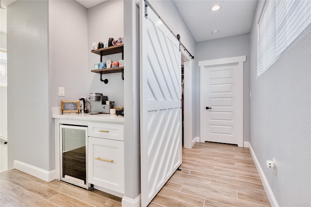 bar with white cabinetry, light wood-type flooring, a barn door, and beverage cooler